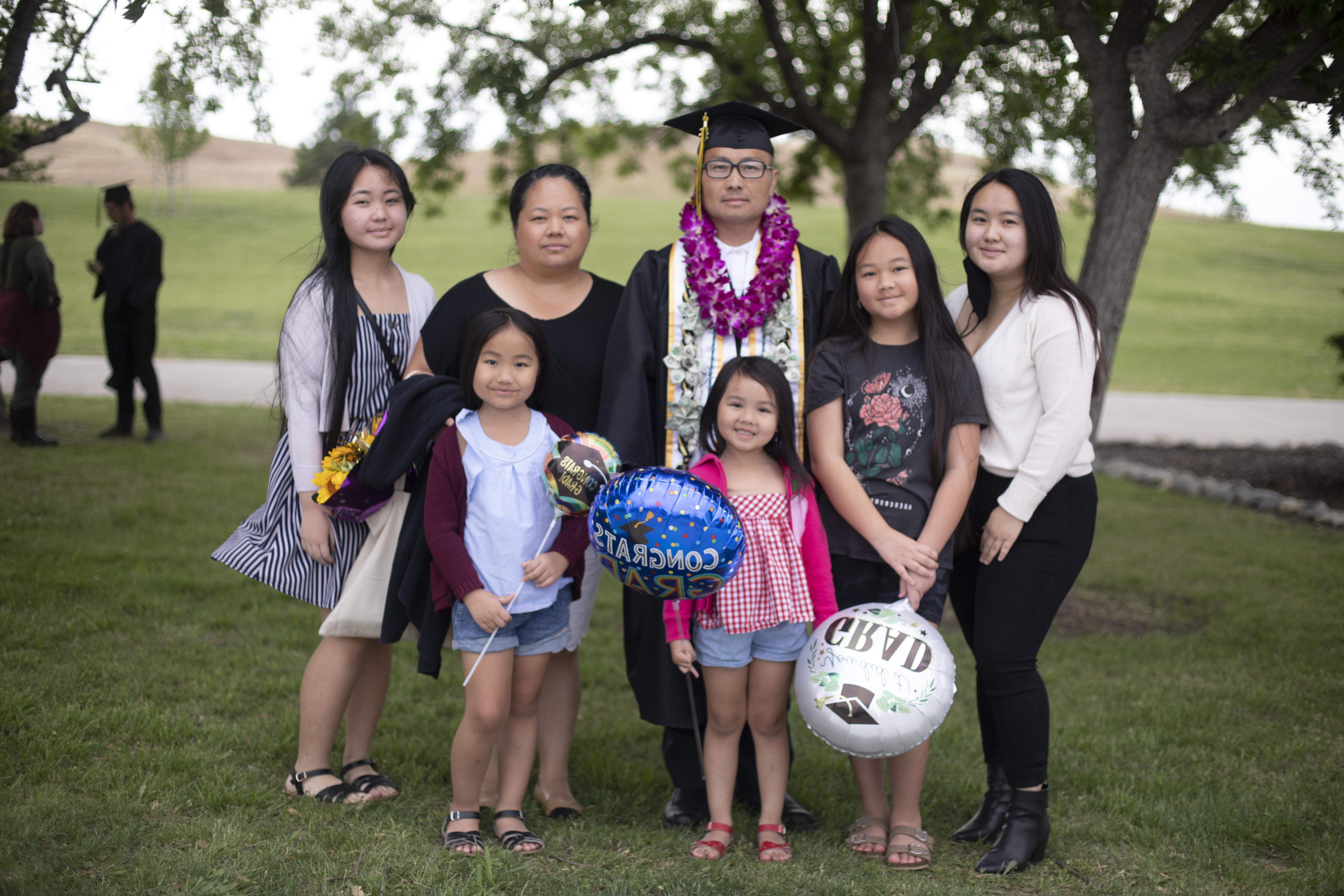 Male student in cap and gown posing with his family